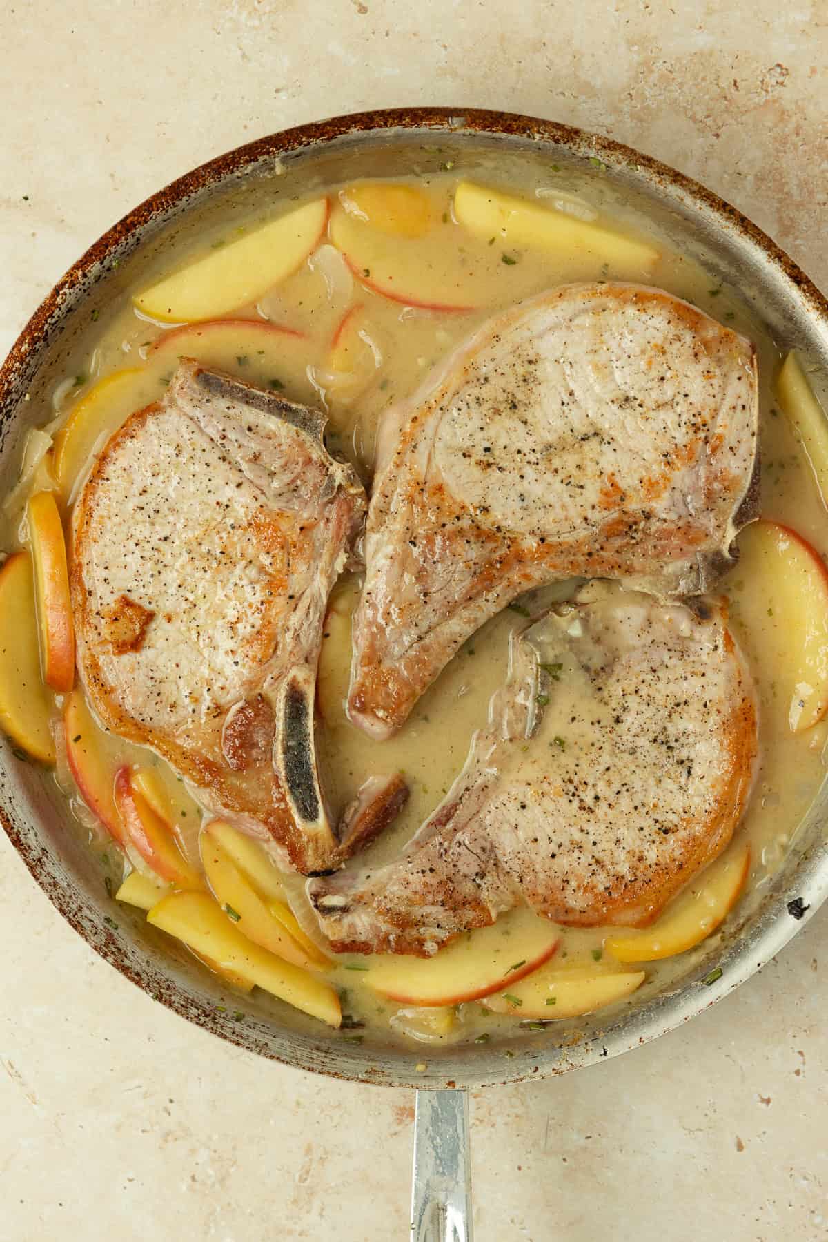 Pork chops added to a skillet with apples and onions.