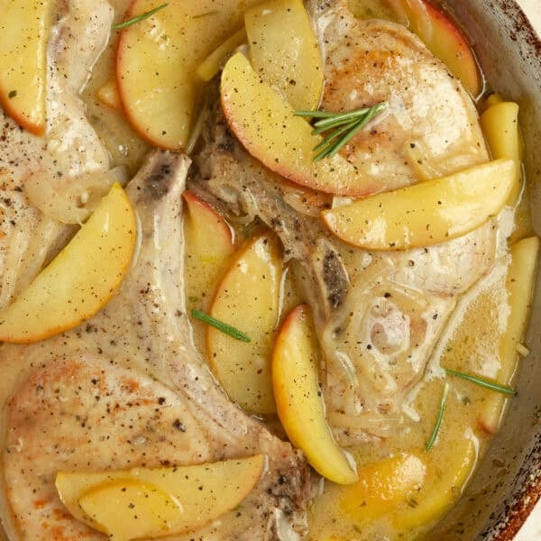 Close up of pork chops with sautéed apples and onions in a pan.