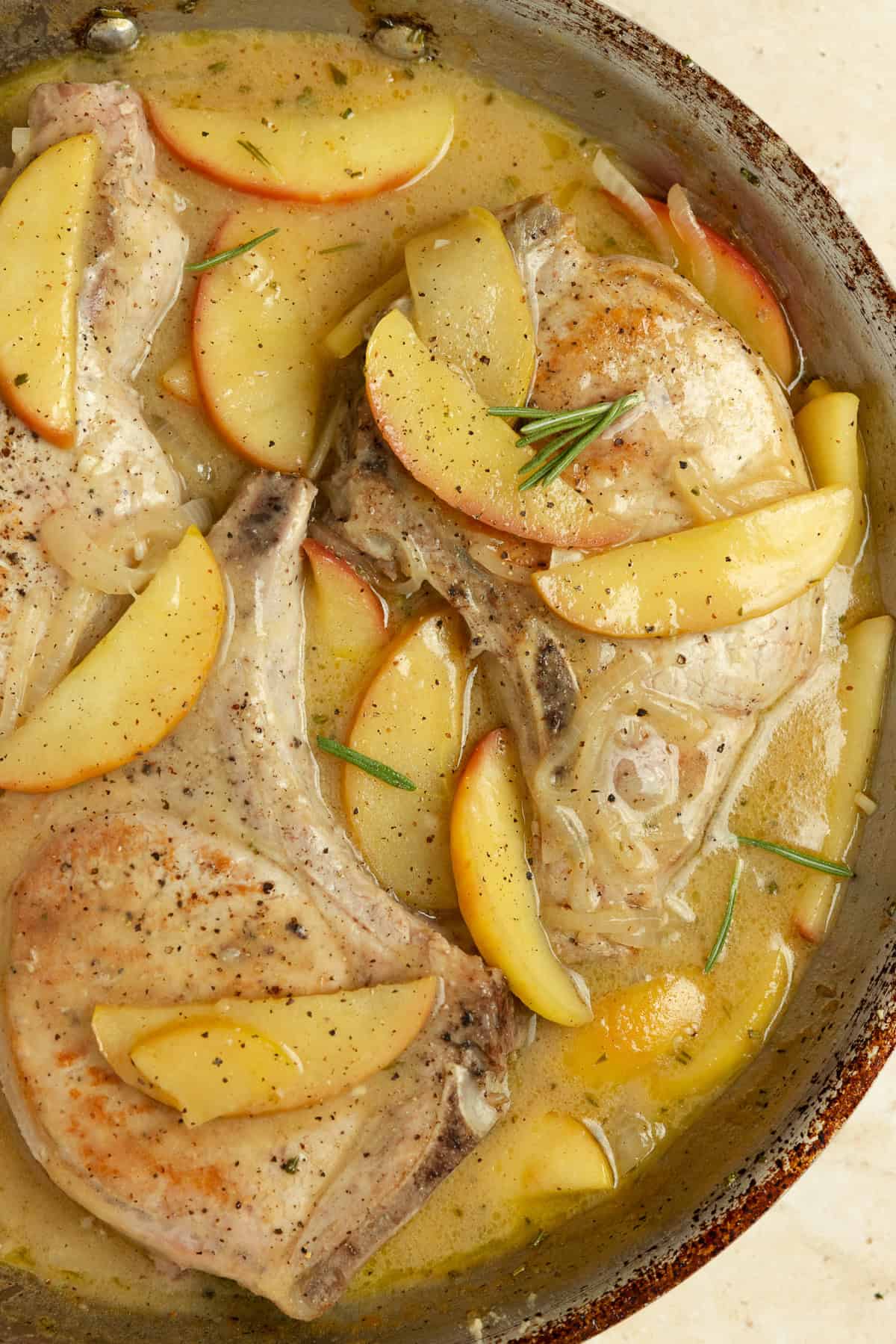 Close up of pork chops with sautéed apples and onions in a pan.