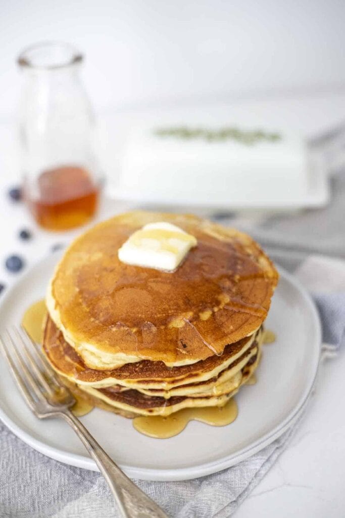 A stack of pancakes with a pat of butter on top coated in maple syrup on a white plate.
