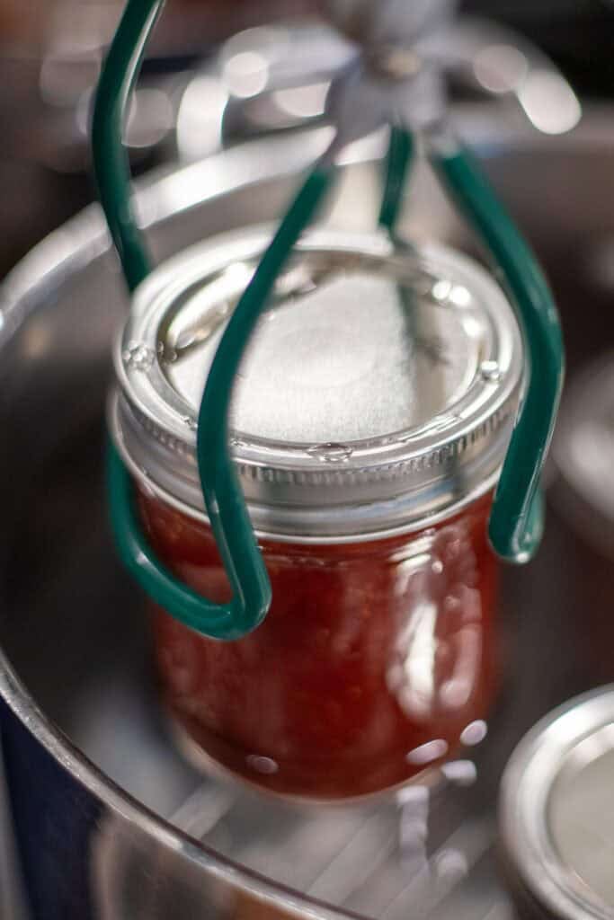 Placing a glass jar of jelly into a water bath canner.