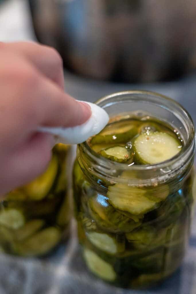Cleaning the top of a glass jar that is filled with pickles.
