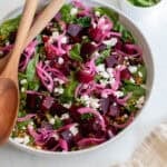 A bowl full of salad with two wooden spoons.