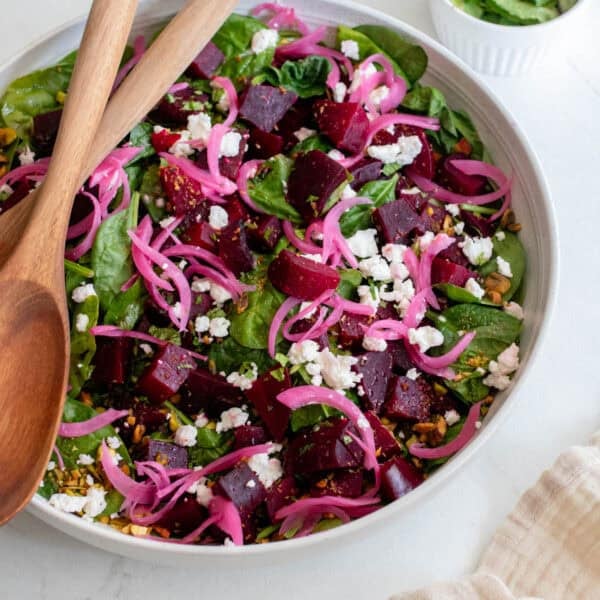 A bowl full of salad with two wooden spoons.