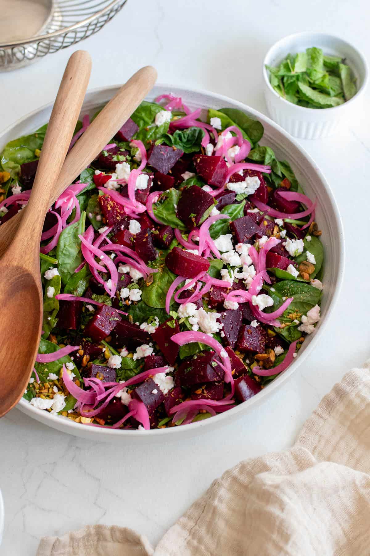 A bowl full of roasted beet salad with two wooden spoons. 