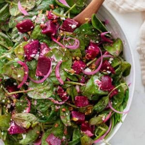A large bowl of salad with two wooden spoons inside.