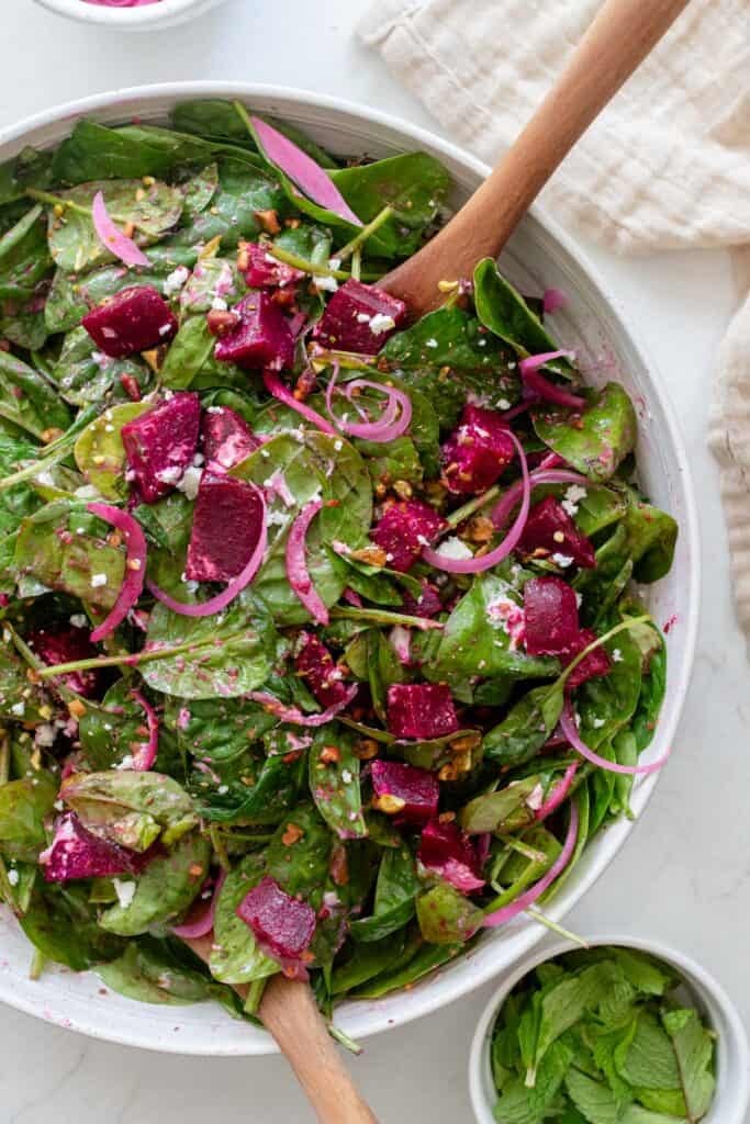 A large bowl of  roasted beet salad with two wooden spoons inside.