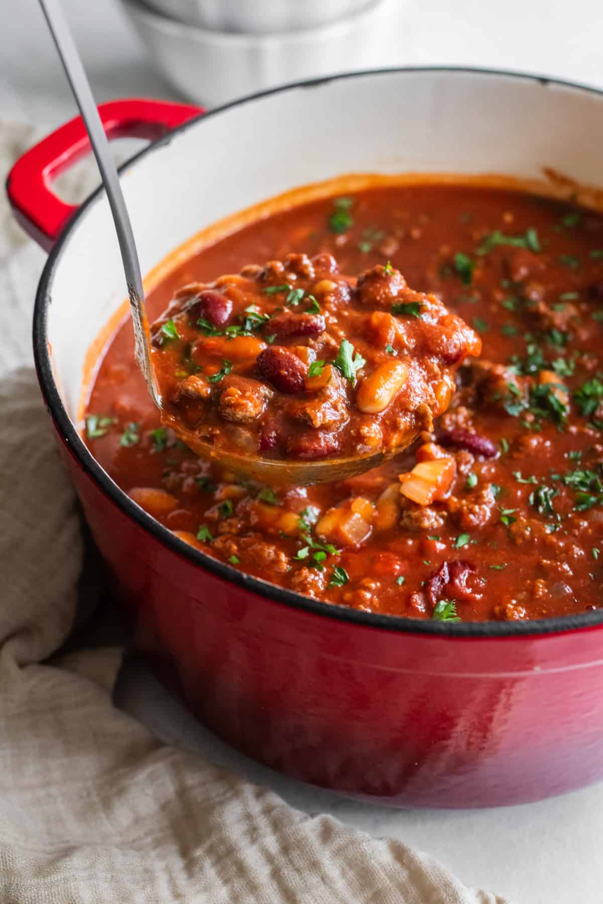 A ladle scooping out chili from a Dutch oven.