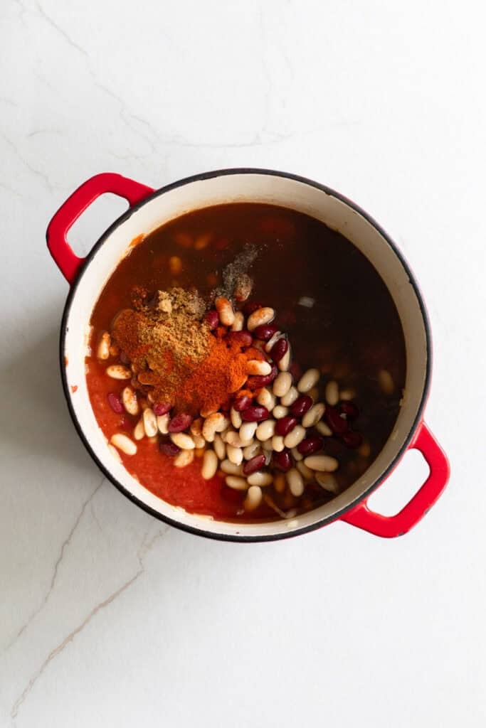 Onions, garlic, beans, spices, and other ingredients in a Dutch oven.