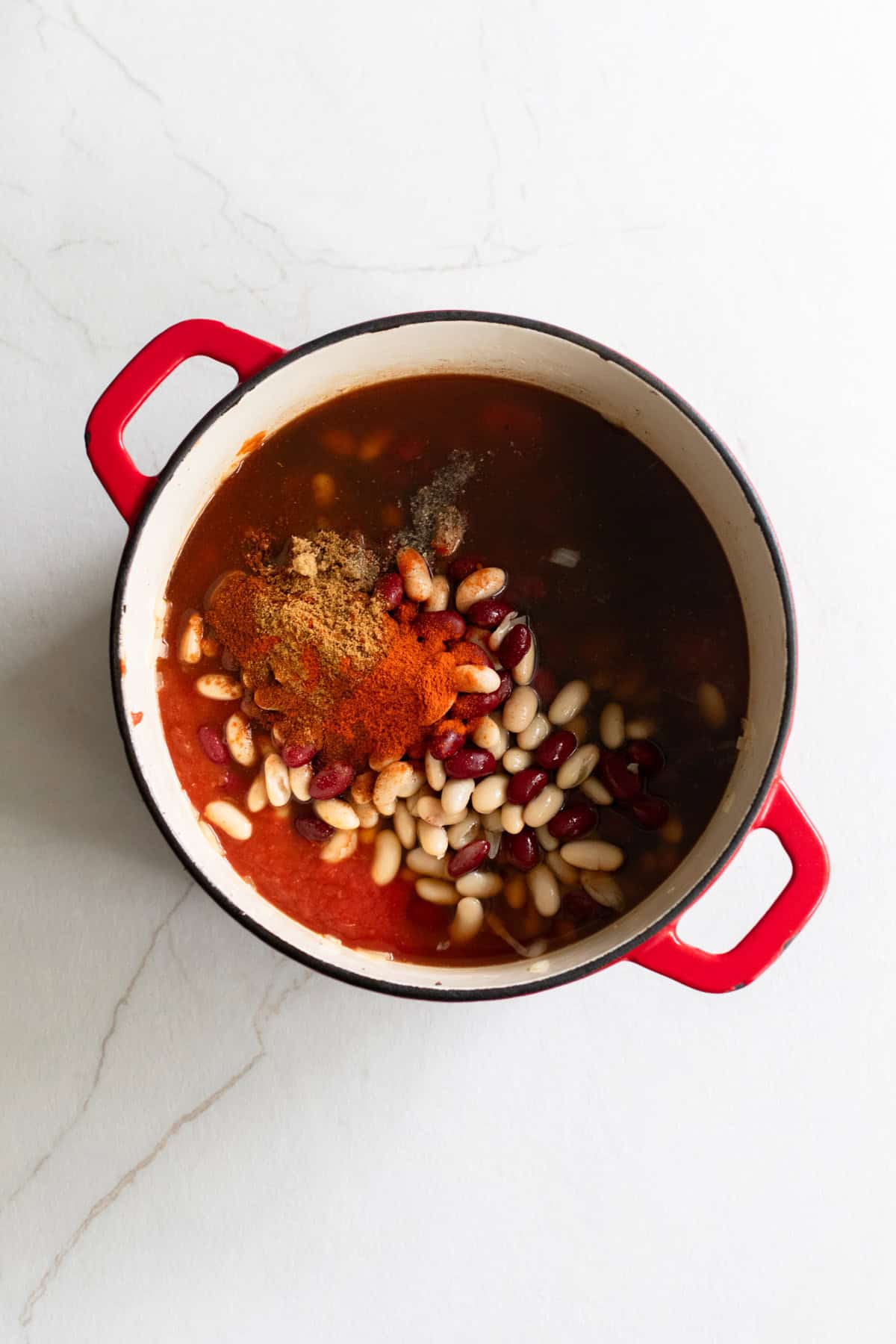 Onions, garlic, beans, spices, and other ingredients in a Dutch oven.