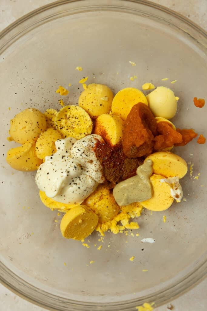 Eggs, mayo, mustard, spices, and pumpkin puree in a glass bowl.