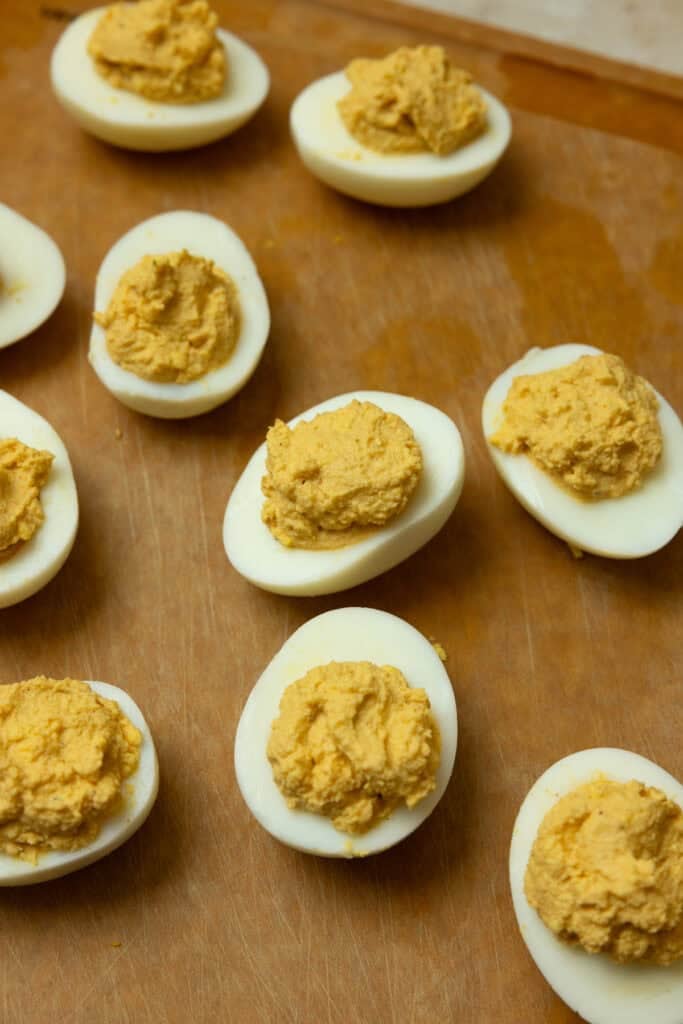 Adding pumpkin egg mixture into halved eggs on a cutting board.