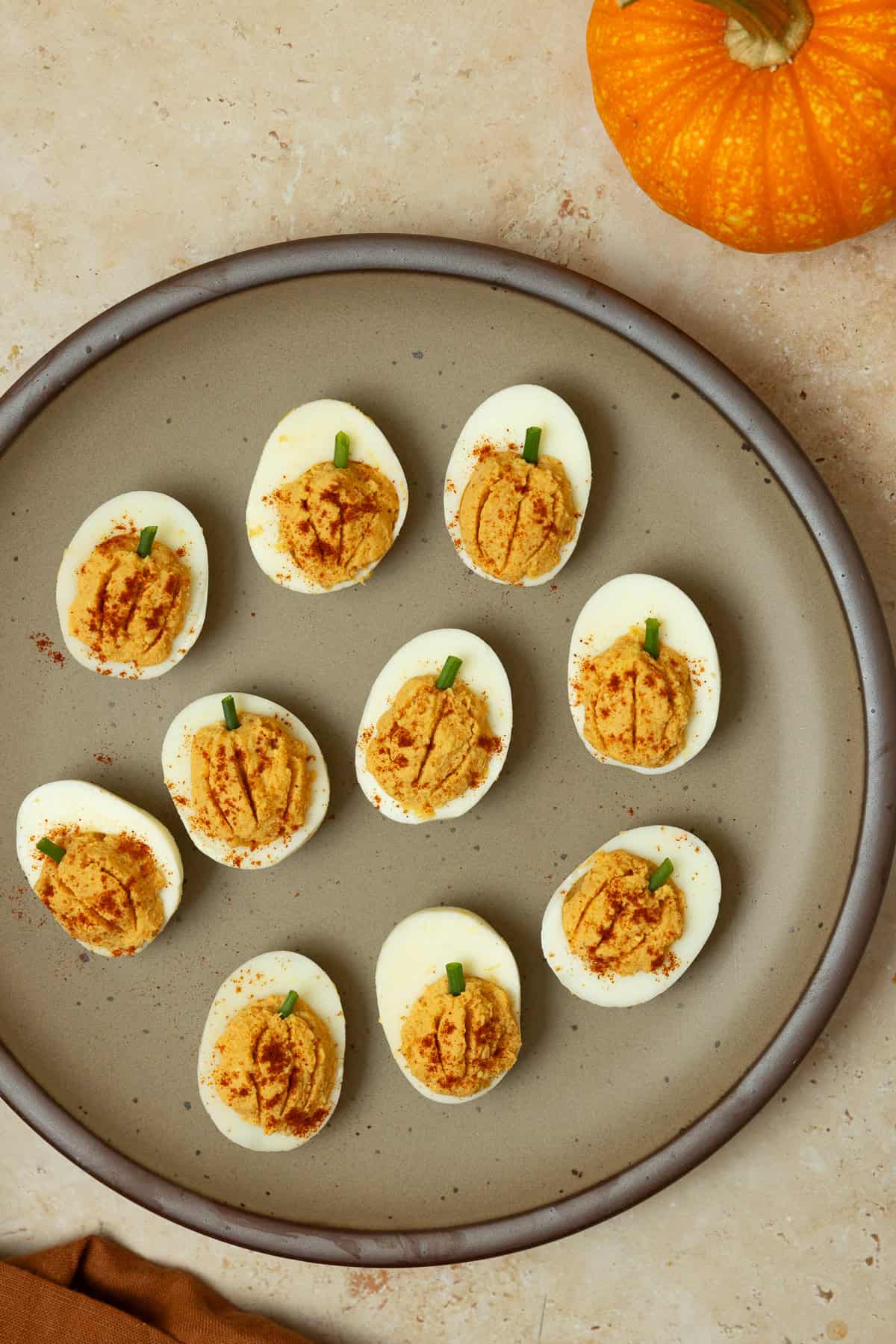 10 pumpkin deviled eggs on a plate with a pumpkin in the background.