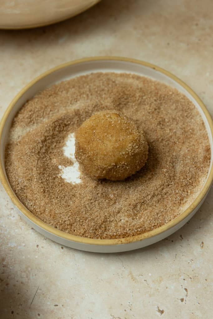 Cookie dough rolled into a sugar mixture on a plate.