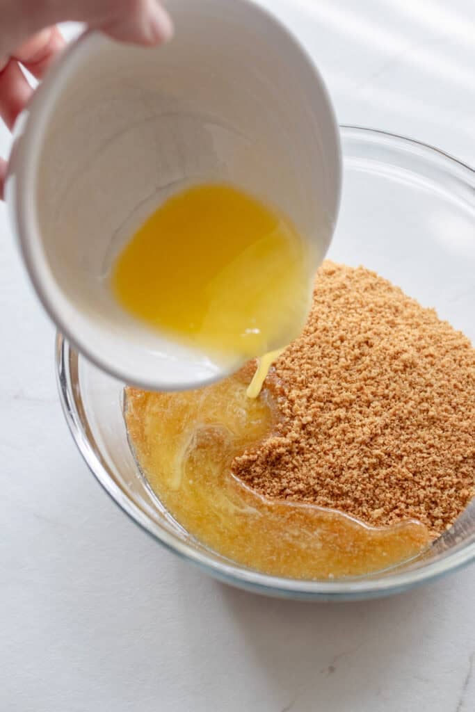 Gingersnap cookie crumbs mixed with melted butter in a glass bowl.