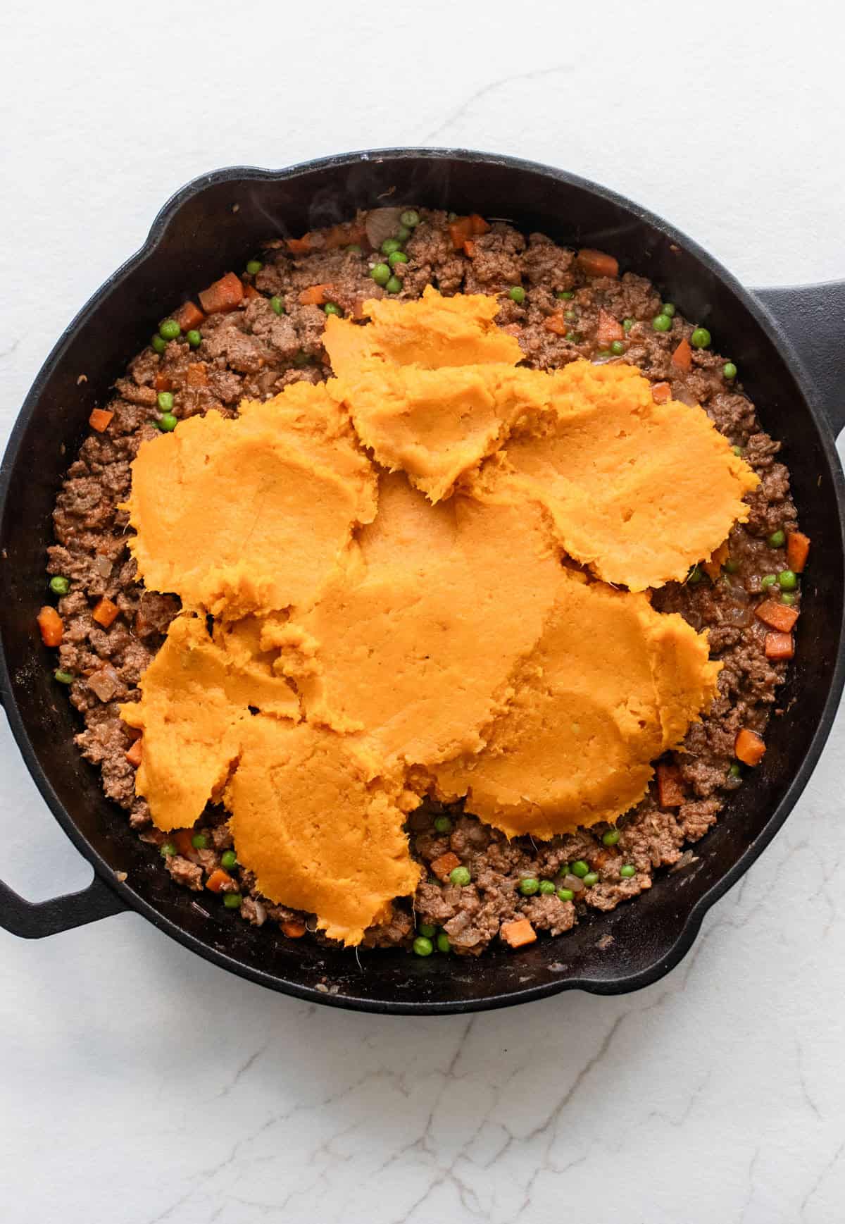 Sweet potatoes on top of ground beef in skillet.