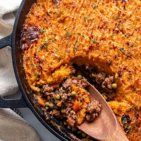 A cast iron pan with a wooden spoon scooping out shepherd's pie.