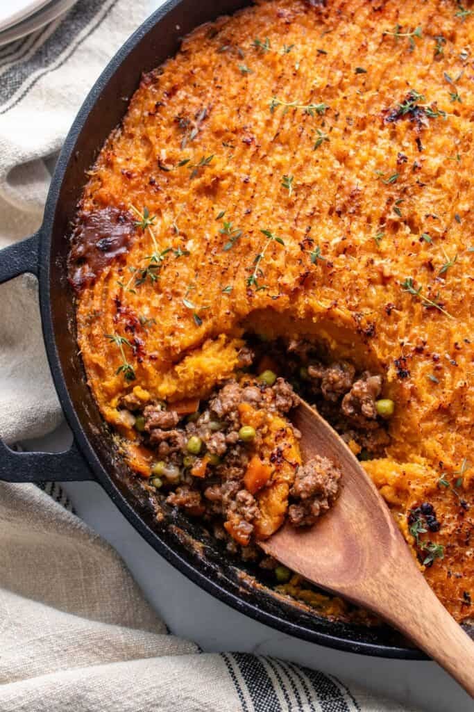 A cast iron pan with a wooden spoon scooping out shepherd's pie.