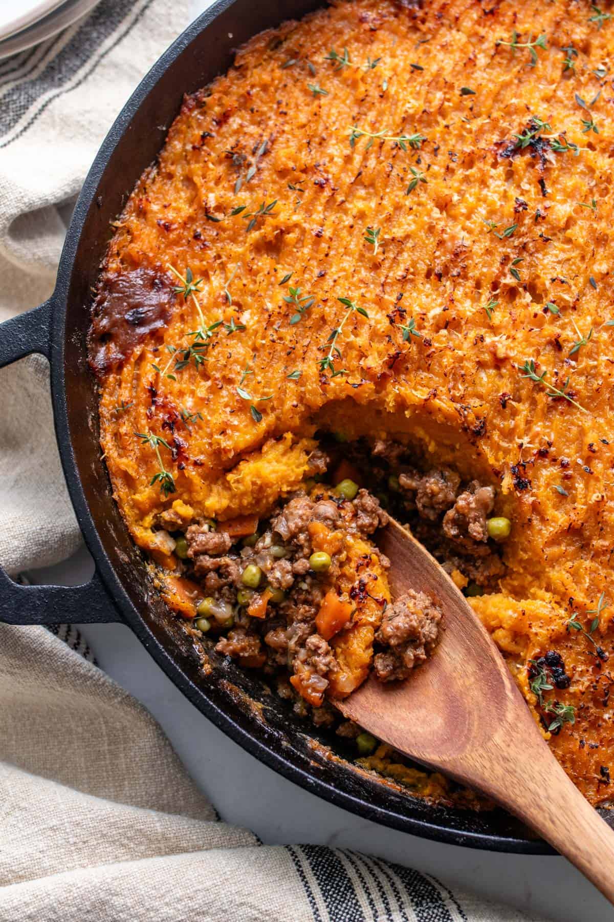 A cast iron pan with a wooden spoon scooping out shepherd's pie.