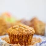 an apple and carrot muffin with the liner pulled down on a decorative plate.