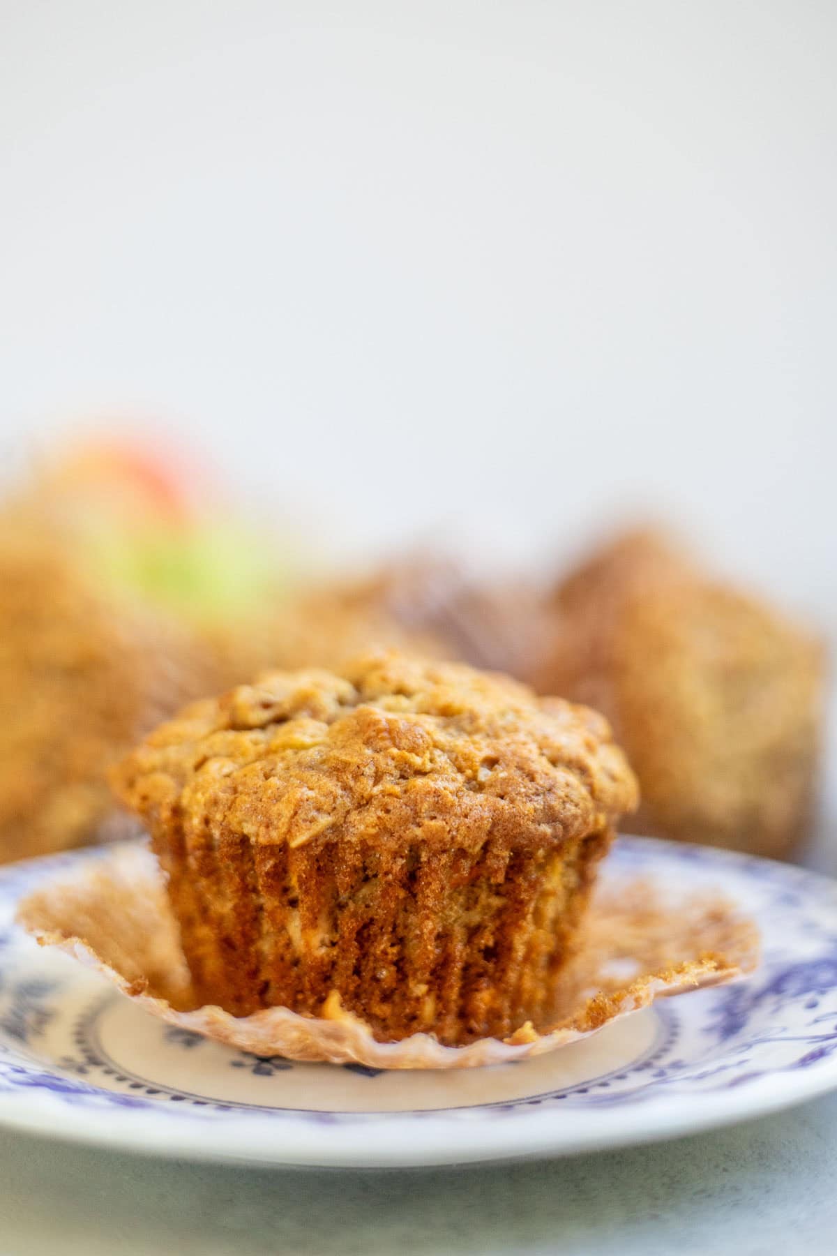 An apple and carrot muffin with the liner pulled down on a decorative plate.