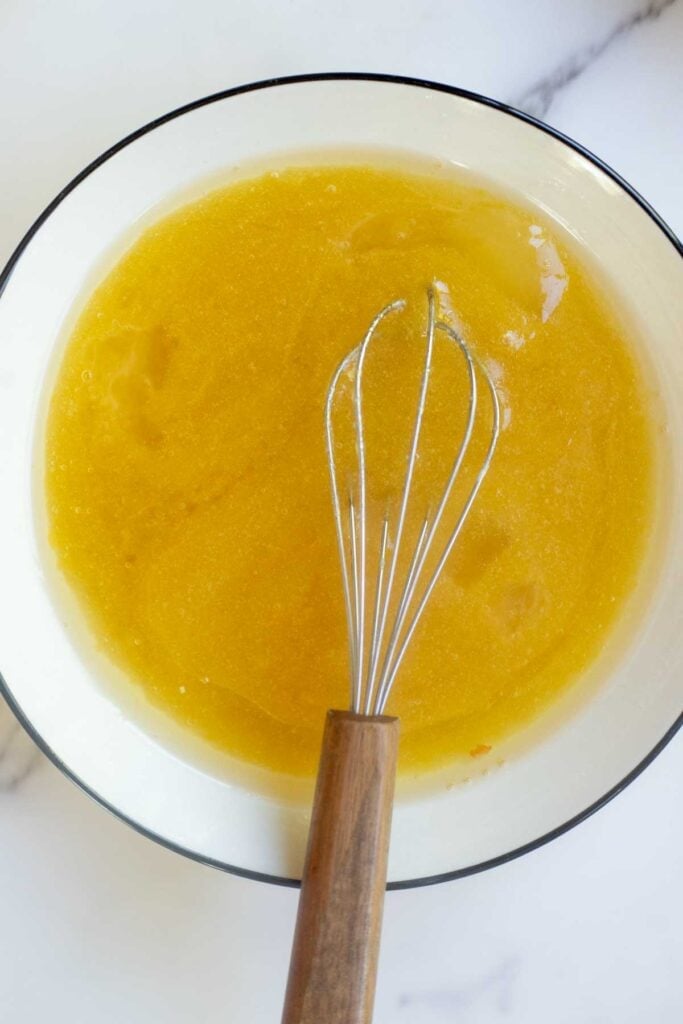 Oil, sugar and eggs mixed together in a white bowl.