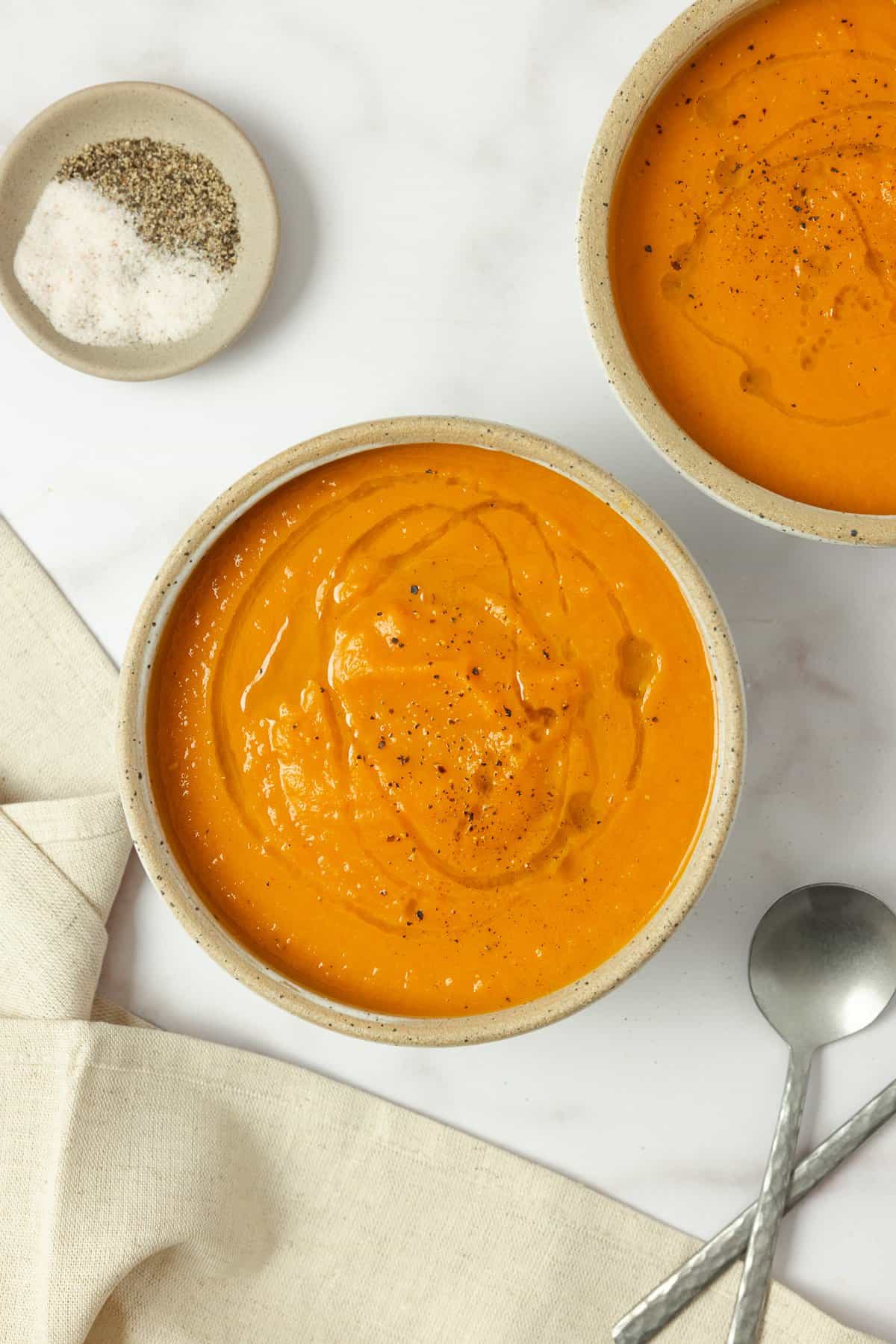Two bowls of carrot ginger soup on the counter.