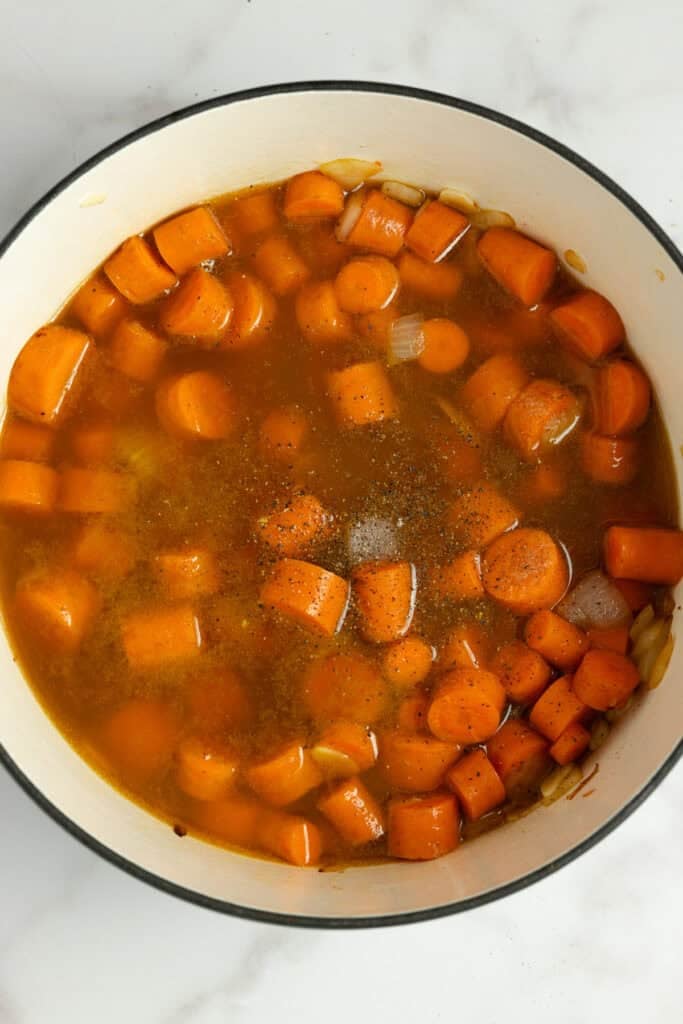 Carrots, broth, onions, and garlic being simmered in a pot.
