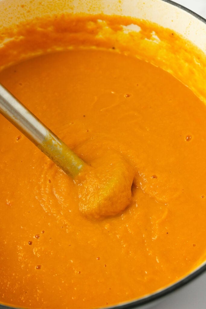 Blending carrot and ginger soup with an immersion blender until smooth.