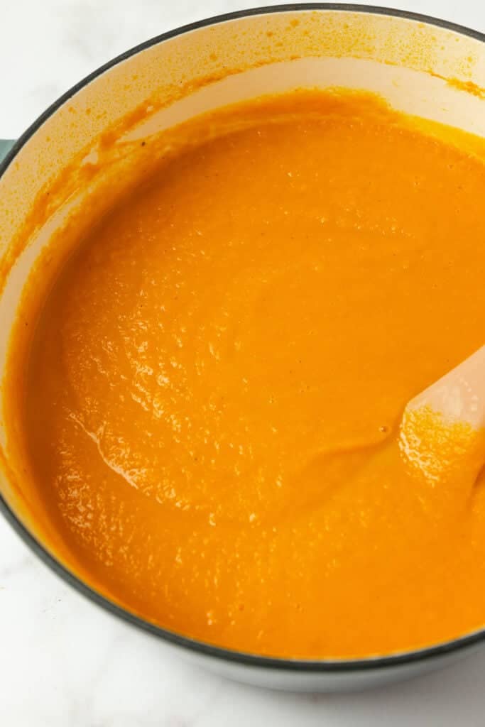Carrot ginger soup in a large pot wit a spatula.