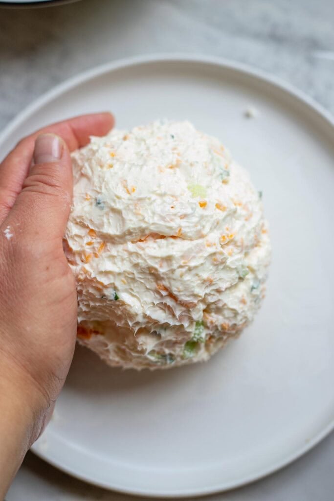A cheese balled formed into a ball on a white plate.