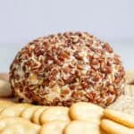 a cheese ball covered in nuts on a cutting board surrounded by crackers.