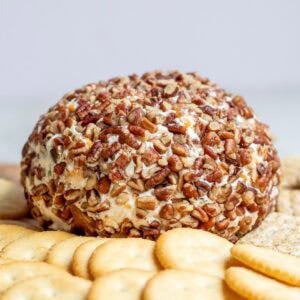 a cheese ball covered in nuts on a cutting board surrounded by crackers.