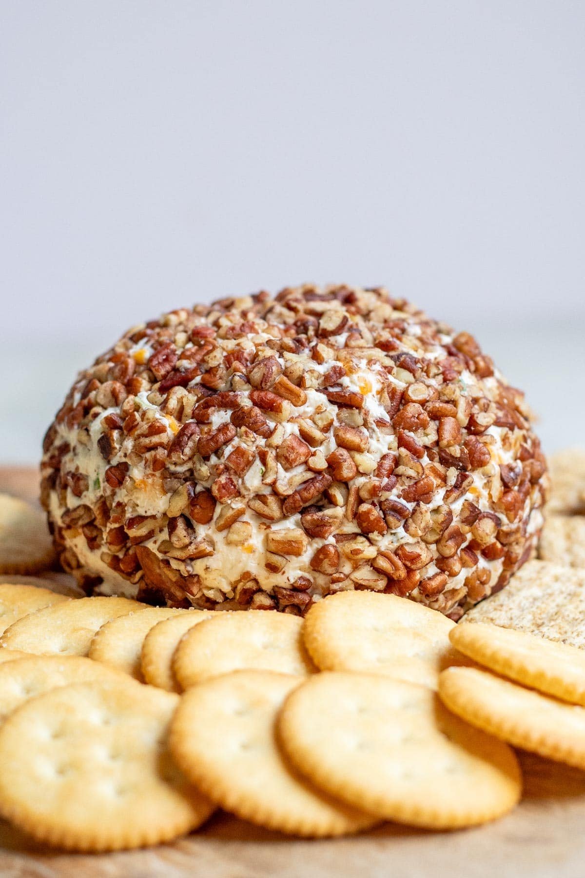 A cheese ball covered in nuts on a cutting board surrounded by crackers.
