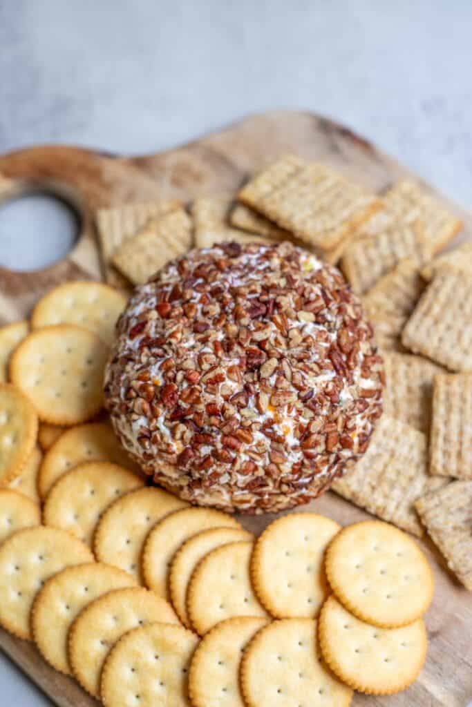 A cheese ball on a cutting board surrounded with crackers.