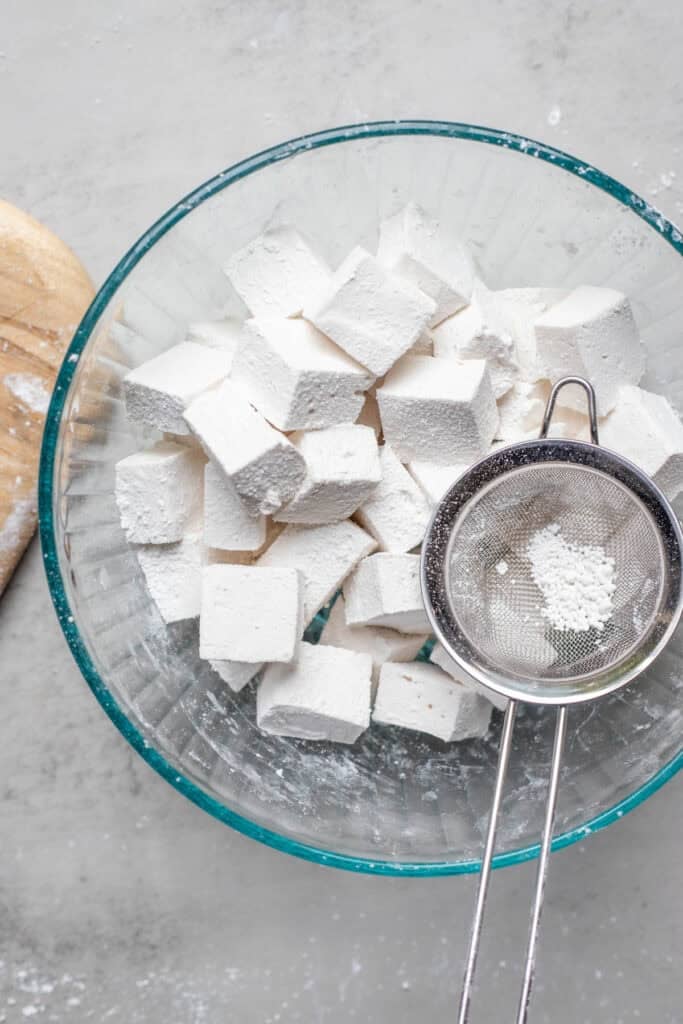 Marshmallow chunks in a glass bowl dusted with powdered sugar and corn starch.