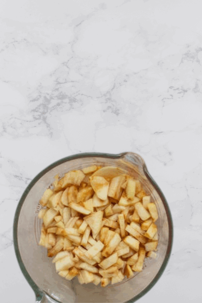 A glass bowl of diced apples on a marble counter.