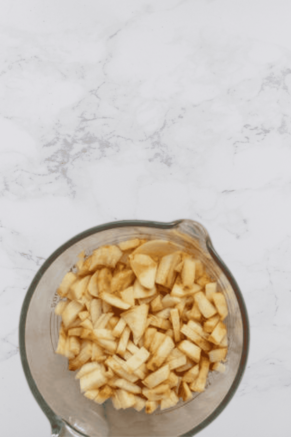 A glass bowl of diced apples on a marble counter.