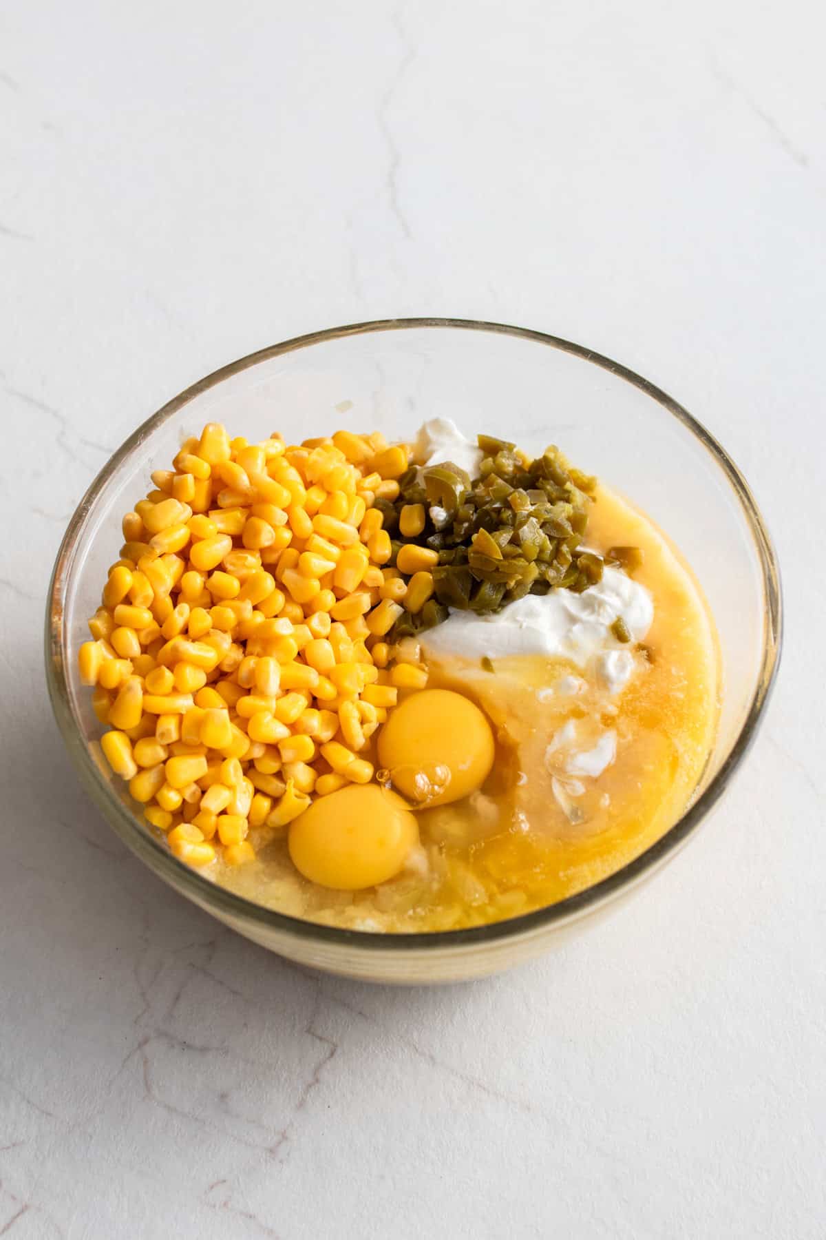 Large bowl filed with eggs, corn, jalapeño, sour cream, and other ingredients.