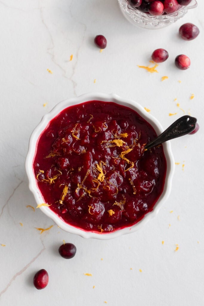 a bowl of cranberry sauce on the counter with a serving spoon in the side of the bowl.