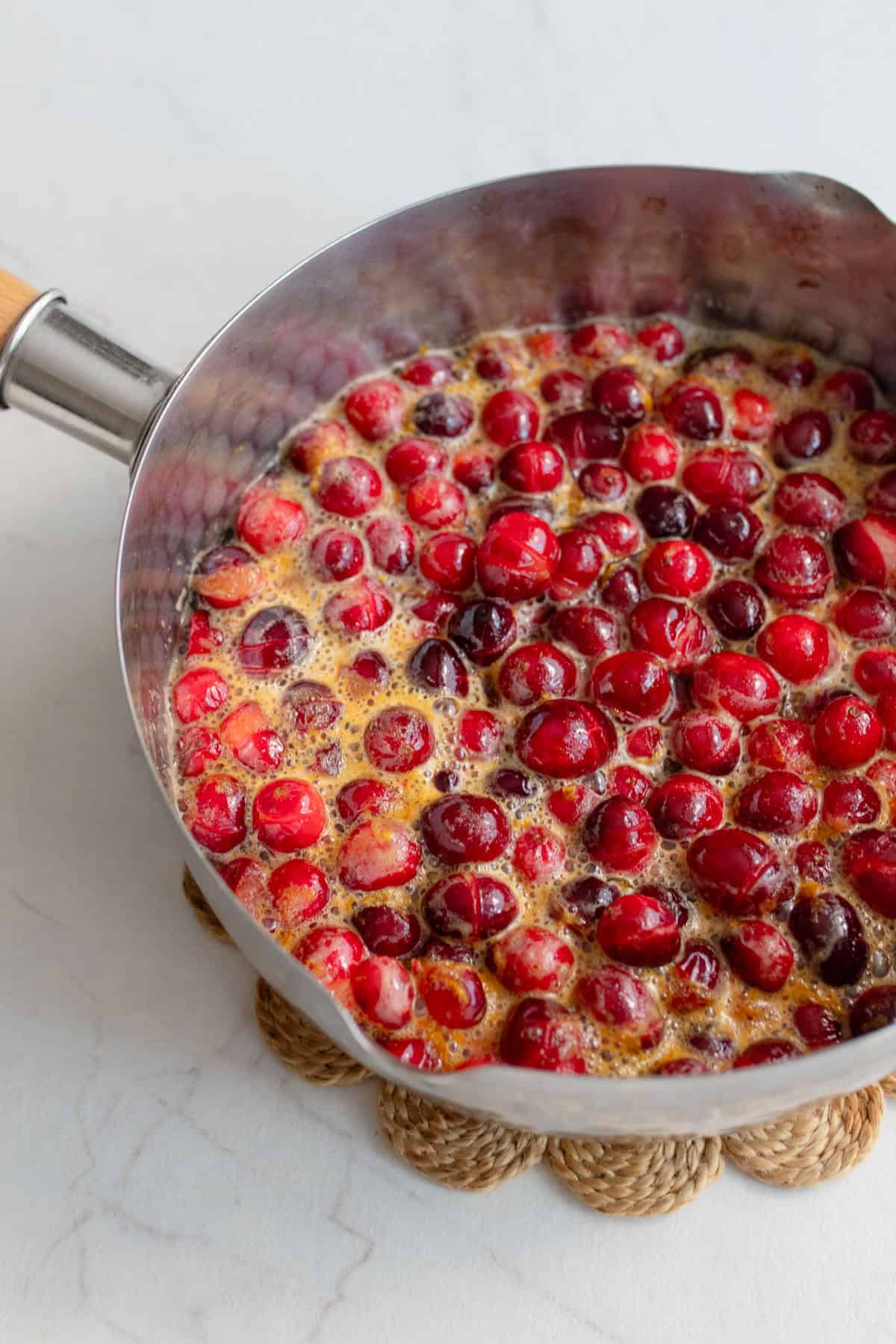 Cranberries with orange zest, maple syrup, and apple cider in a pot.