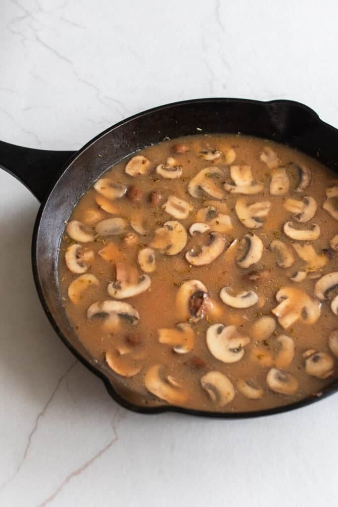Broth mixture added to sautéed mushrooms in a skillet.