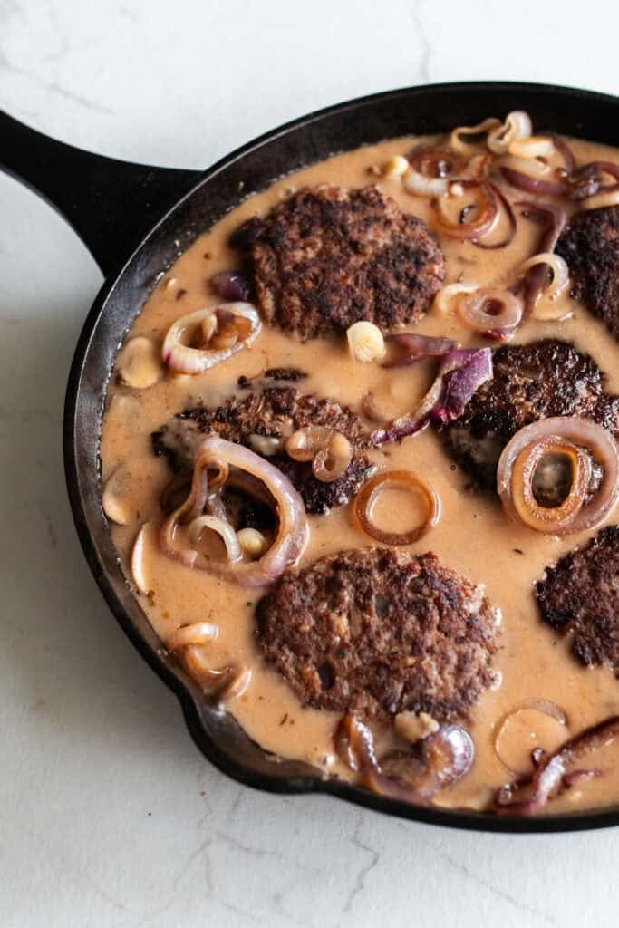 Simmering Salisbury steak patties, onions, mushrooms, and gravy in a skillet.