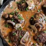 Salisbury steak with onions, mushroom, and gravy in a skillet.