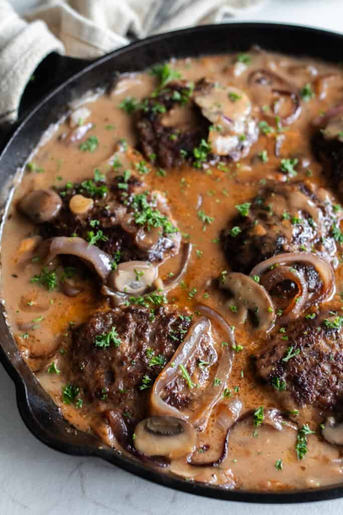 Finished Salisbury steak with onions, mushroom, and gravy in a skillet.