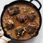 Salisbury steak simmering in gravy with onions and mushrooms in a cast iron skillet.