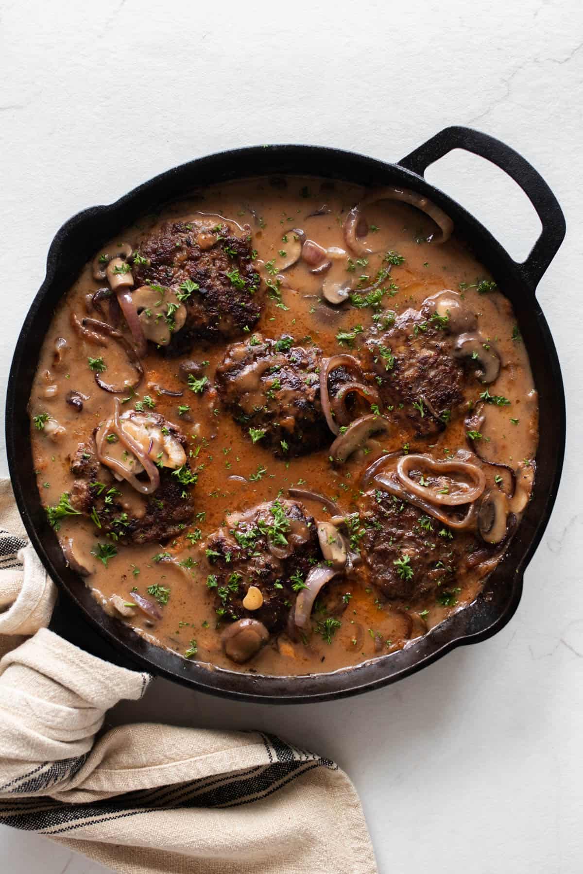 Salisbury steak simmering in gravy with onions and mushrooms in a cast iron skillet.