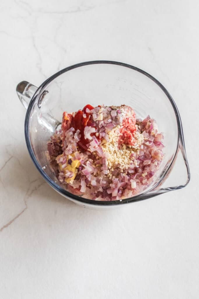 Adding diced onion, garlic, and spices to aground meet in a bowl.