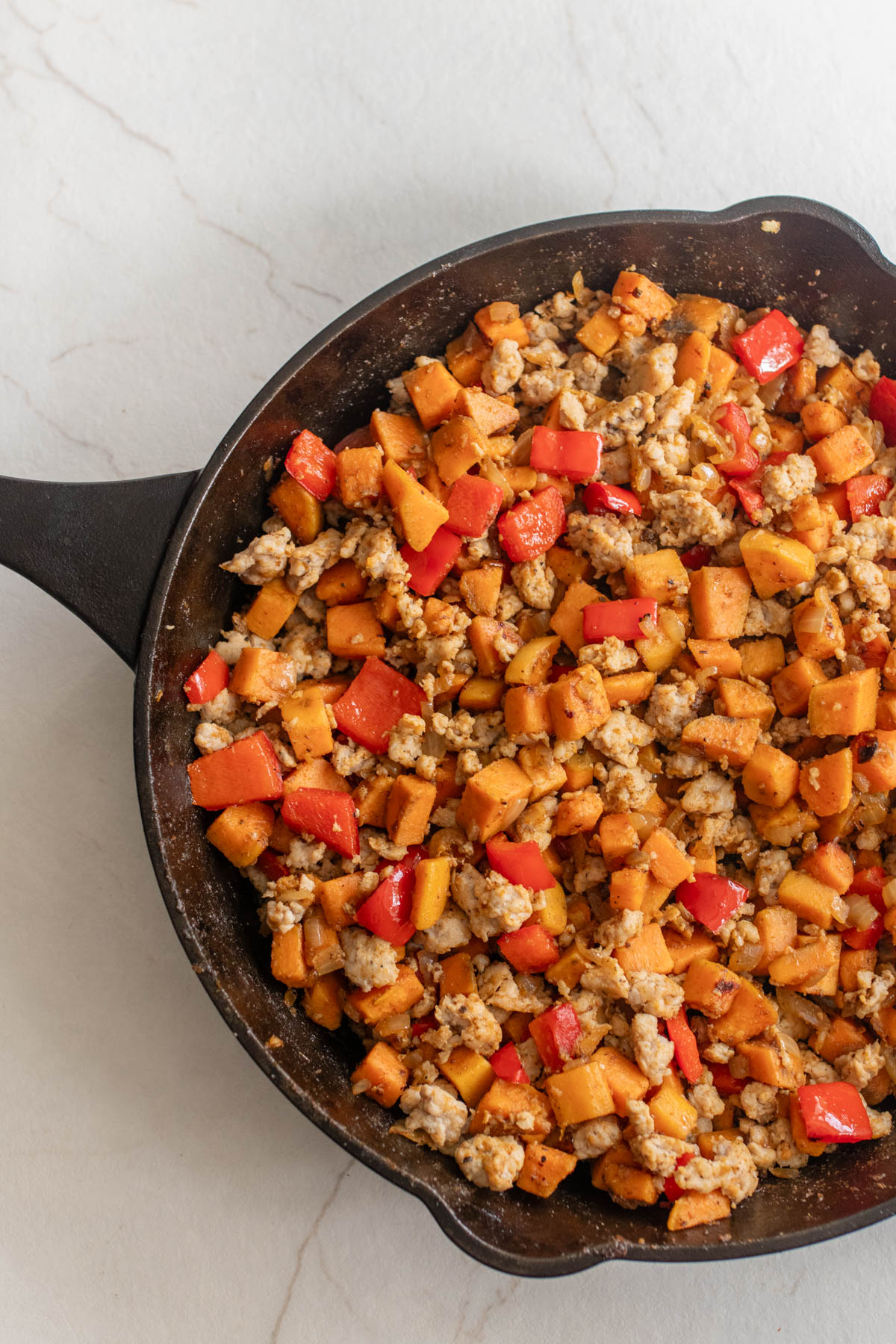 Sweet potatoes, bell peppers, onions, and sausage cooked together in a cast iron skillet.