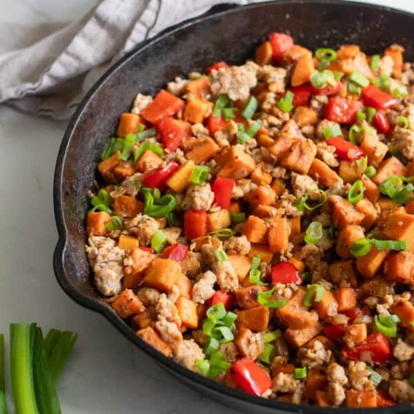 sweet potato hash topped with green onions in a cast iron skillet.